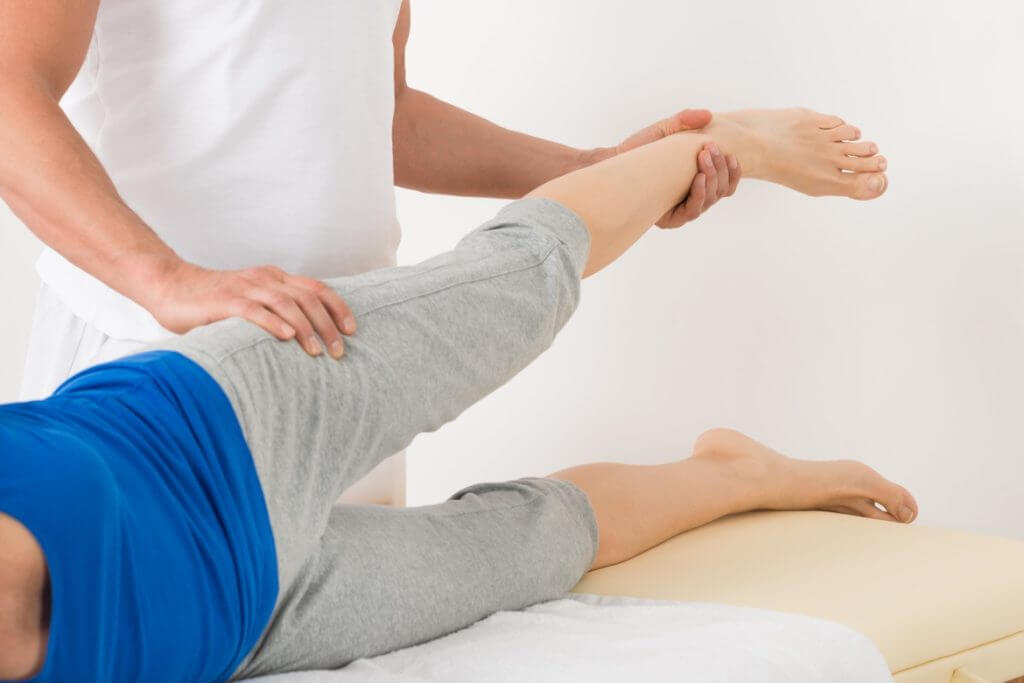 Frau liegt auf der Seite, ein Bein ruht auf der Liege, das zweite wird von einem Mann gehalten Frau liegt auf der Seite, ein Bein ruht auf der Liege, das zweite wird von einem Mann gehalten